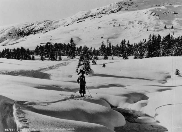 Avfotografert postkort. En enslig skiløper står ved en åpen bekk i et snødekt vinterlandskap i nærheten av Gålå høyfjellshotell.
