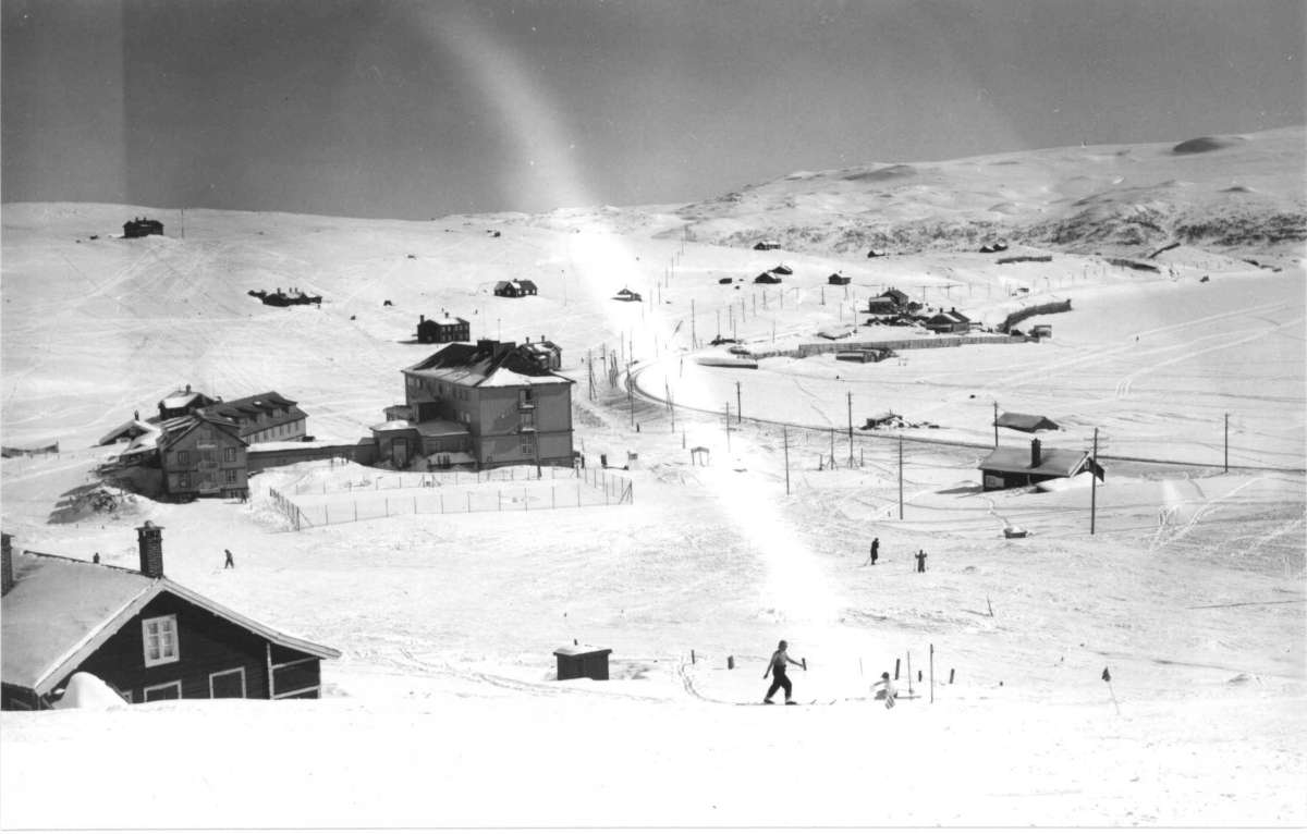 Ustaoset, Hallingdal. Vinterlandskap. Fjellområde med hyttebebyggelse. Skiløpere går i løypene. Til høyre i bildet ses jernbanen.