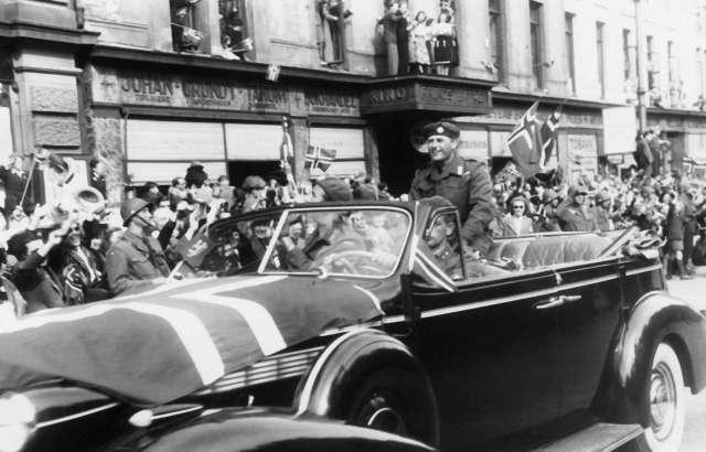 Fra Oslo under fredsdagene i 1945.
Den 13.mai kommer Kronprins Olav tilbake.
Kortesjen kjører oppover Karl Johans gate i retning Slottet.Kronprinsen sitter på kalesjen og hilser til de fremmøtte.