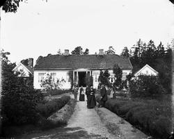 Gruppeportrett, persongruppe foran våningshus, ukjent sted. 