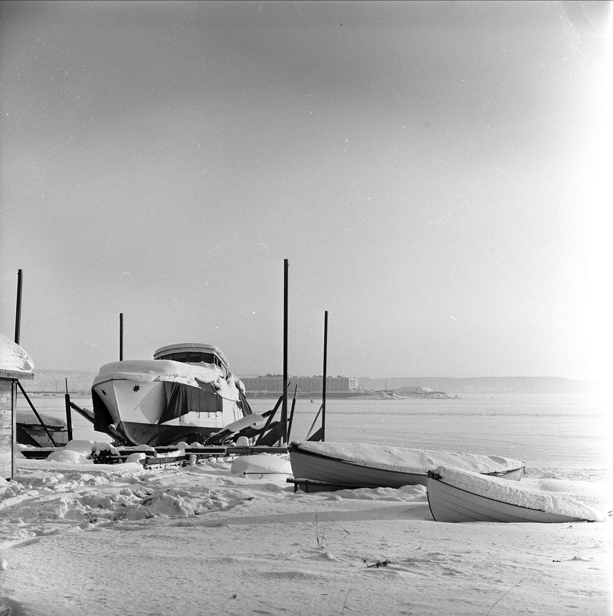 Div. glimt fra Hamar i forbindelse med NM på skøyter, 15.01.1963. Islagt havn med båter. Båt med tretak dekket av snø. (Spissbåt fra Mjøsa.)