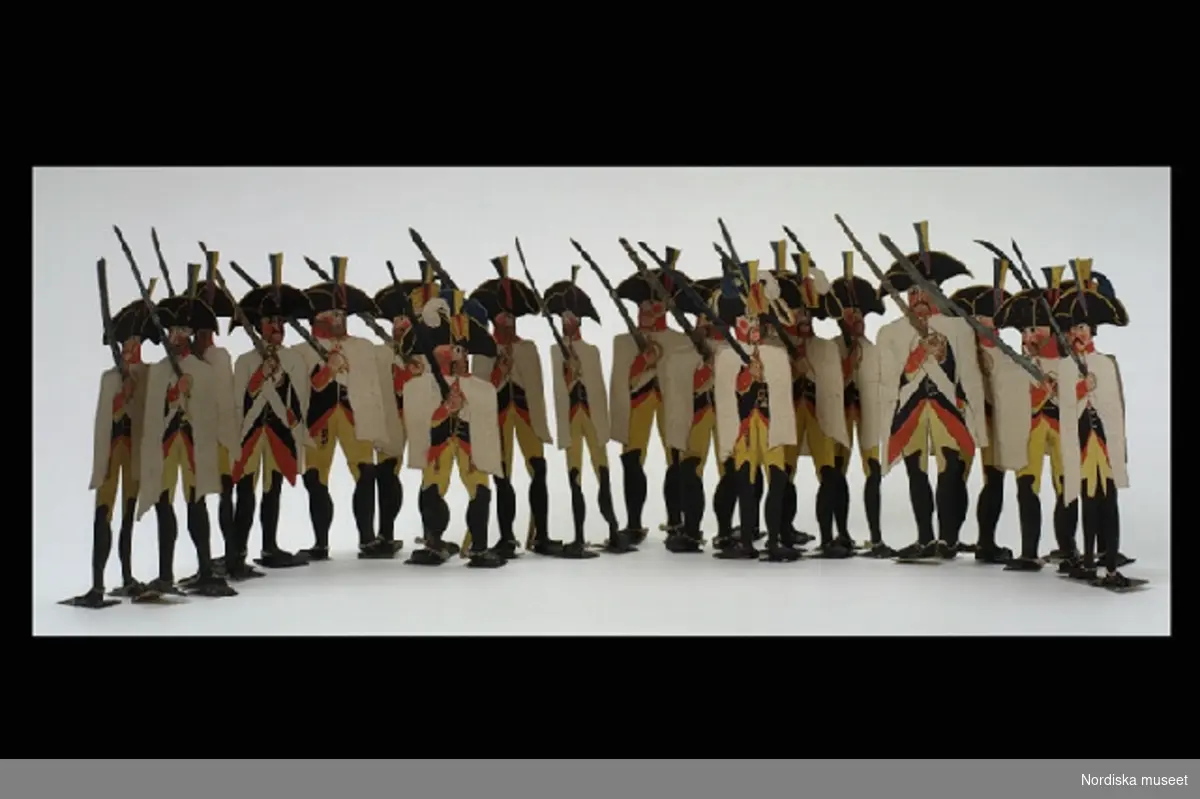 Inventering Sesam 1996-1999:
H 12 cm
20 st soldater av papper, målade med vattenfärg. Mörkblå uniformsjacka, bula byxor, svarta höga stövlar, vit slängkappa och trekantig svart hatt. Soldaterna har dragit sina sablar och håller dem  uppsträckta. Påteckningar på dockora " Gonsaga", "Ganganelli" mm. 
Tillhör dockteater se inv 191.511. Har brukats på Lilla Främsbacka, Stora Kopparbergs sn, Dalarna.
Birgitta Martinius 1996