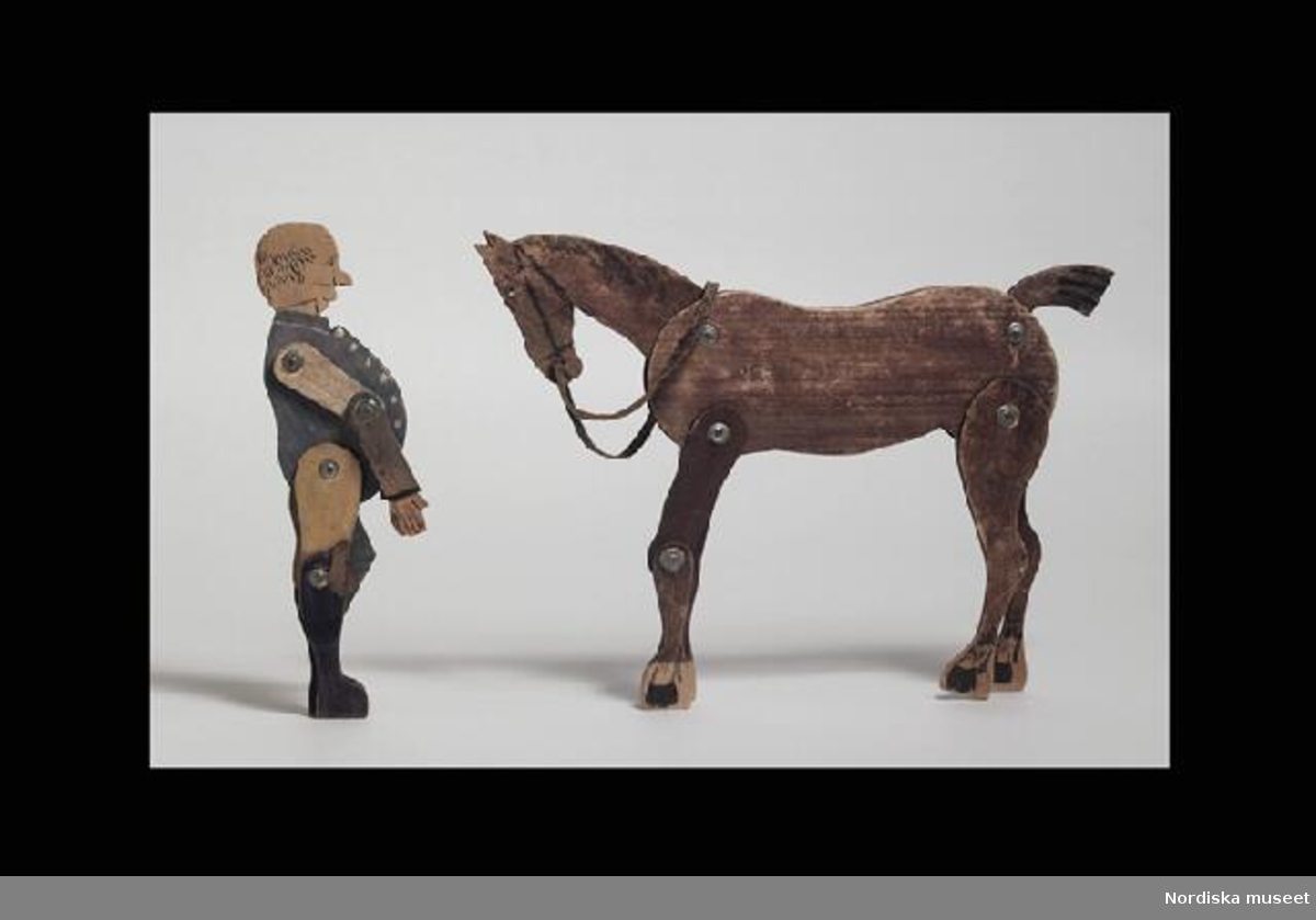 Inventering Sesam 1996-1999:
a) Häst H 28 cm
b) Ryttare H 22,5 cm
Ryttare med häst av tunna träskivor, betsade, lemmar och huvuden ledade.
a) Hästen brun med töm av läder.
b) Ryttare med påmålad blågrön ridfrack och svarta ridstövlar.
Troligen brukad av givarna, födda runt 1890-tal.
Skall troligen föreställa Calle Rask. 
Jmfr liknande figur (Calle Rask) inv.nr 267.536, 268.388 och 323.821 
Leif Wallin feb 1998