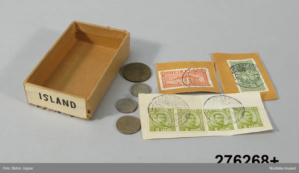 Huvudliggaren:
"Mynt, frimärken, isländska; i brun pappask; 4 mynt, 2 st 10 aur, 1 st 1 krona; 6 st frimärken, 4 st 5 aur, 1 7 aur, 1 20 aur; etikett 'Island'. Mått ask 5 x 8 cm. G 1/7 1966 av Svenska Skolmuseet, Stockholm."