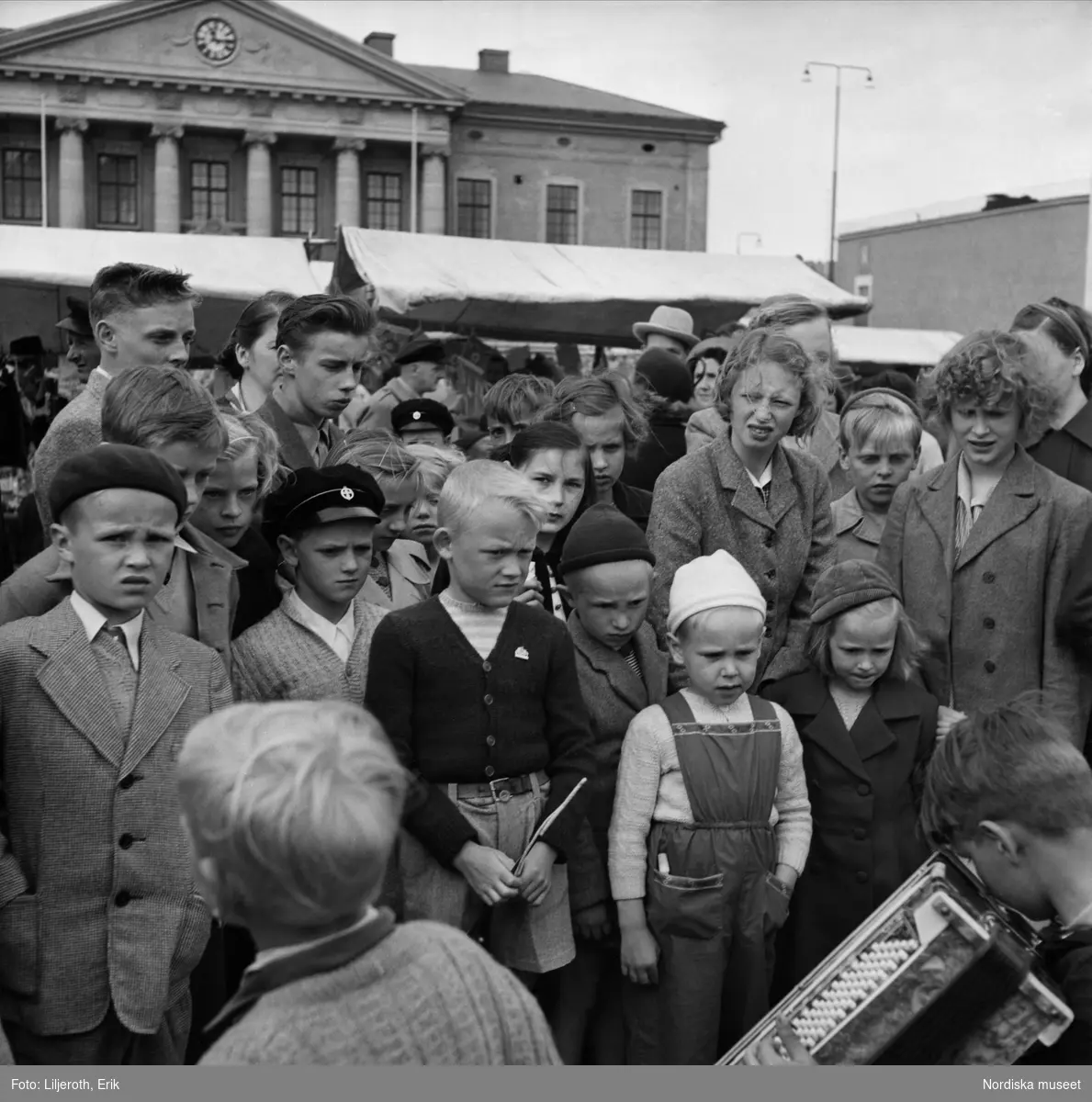 En samling ungdomar som lyssnar på en pojke som spelar dragspel