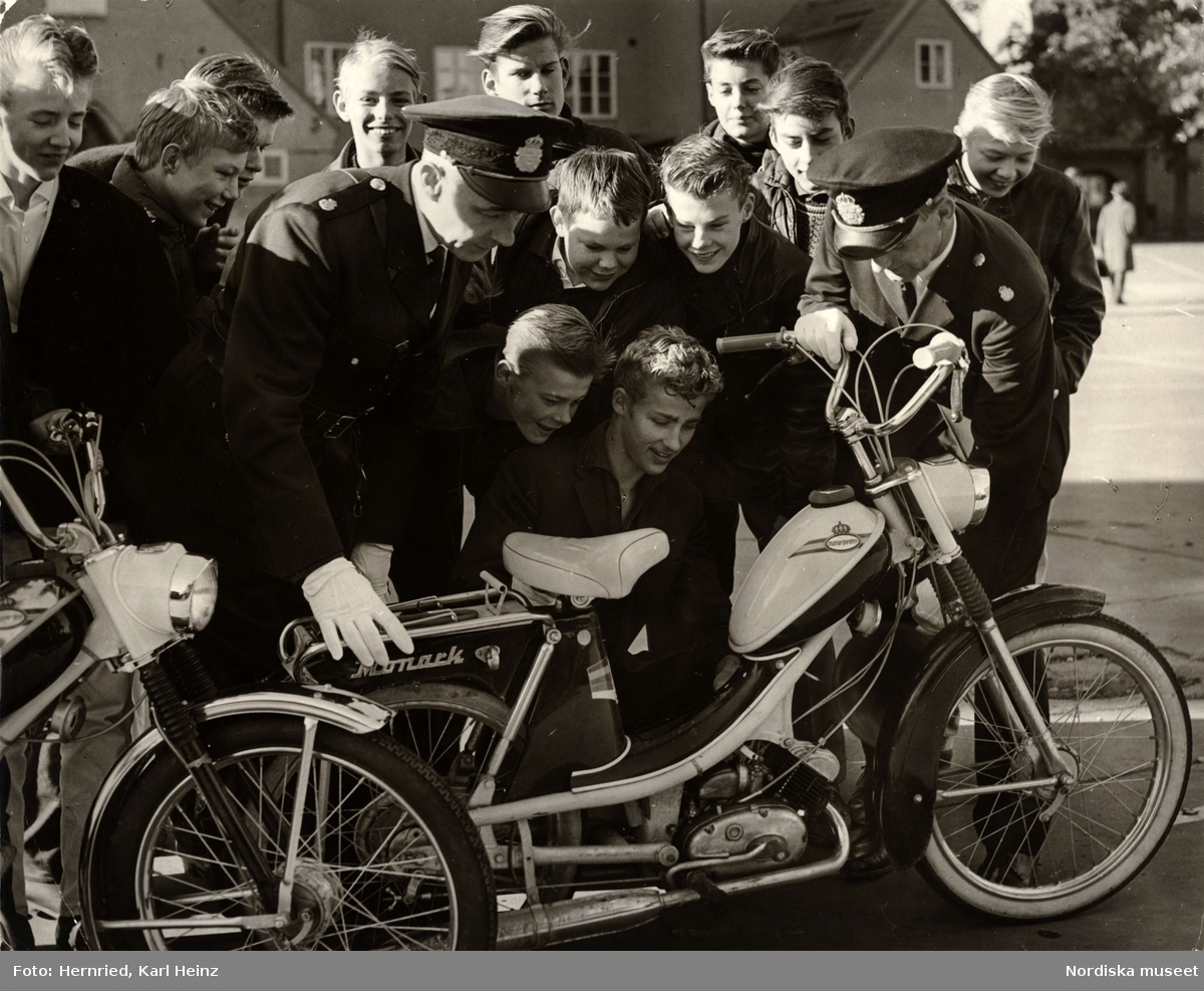 Polis i skola. Två polismän och en grupp pojkar undersöker en moped av märket Monark (monarpeden).