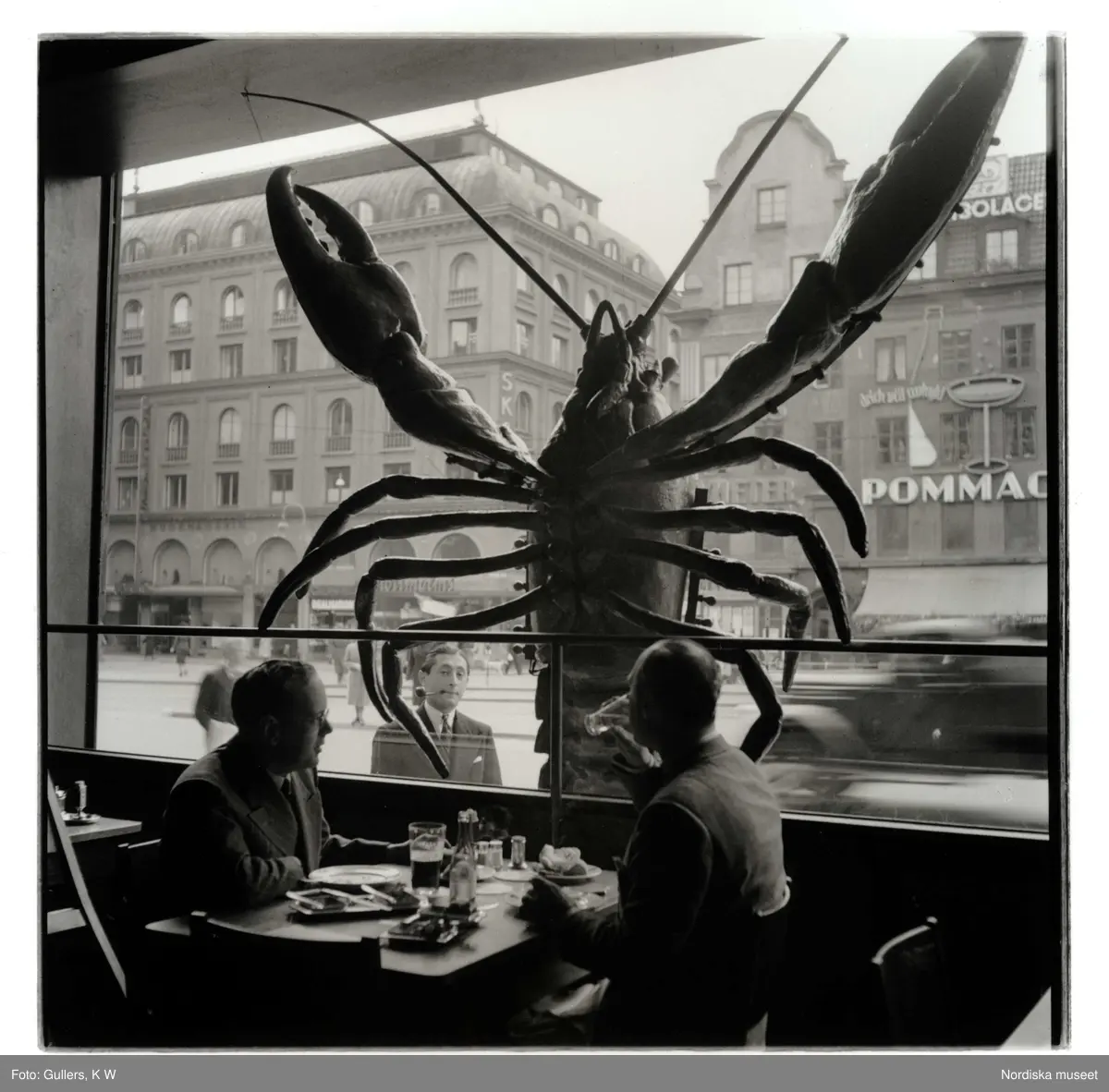 Restaurang Sturehof, Stockholm. Kräftpremiär. En stor kräfta dekorerar fönstret. En man med pipa tittar in genom fönstret. I förgunden två män vid restaurangbord.
