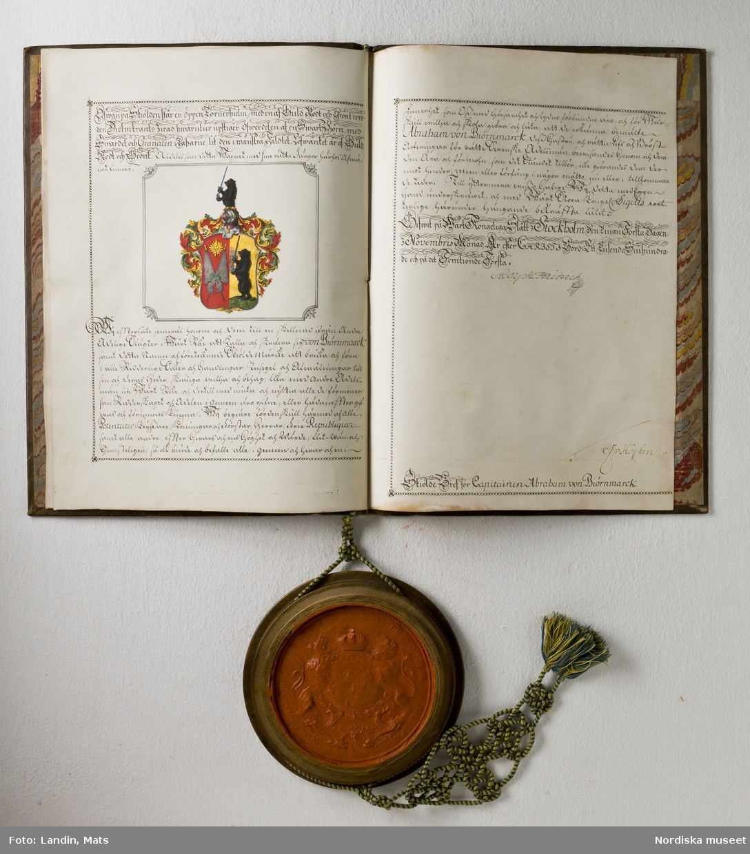 Adelsbrev för kapten Abraham von Björnmarck signerat 1751 av Adolf Fredrik. Sköldebrev. Fyra pergamentsblad, brunt skinnband med guldprägling. Sigill i träkapsel.