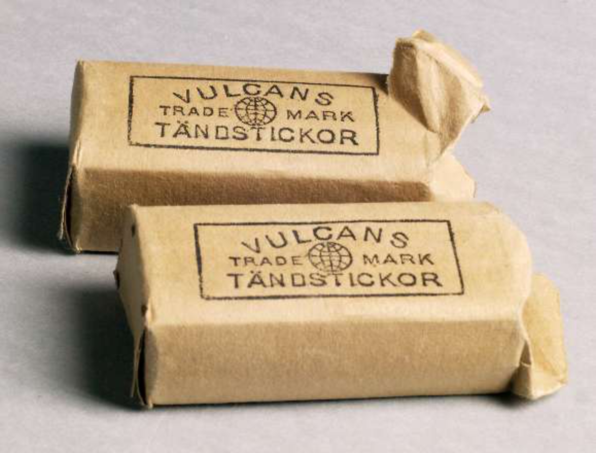 Två förpackningar av gulnat papper, tryckt text: VULCANS TÄNDSTICKOR, TRADE MARK. Innehåller tändstickor.