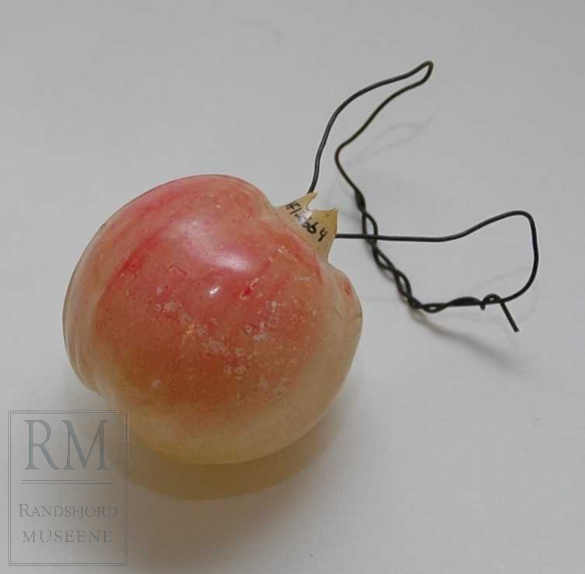 Form: rundt, som et eple. Orginalt oppheng er muligens gått sund. Oppheng laget av fyrstikk og ståltråd. Bare en side har rødmaling.

