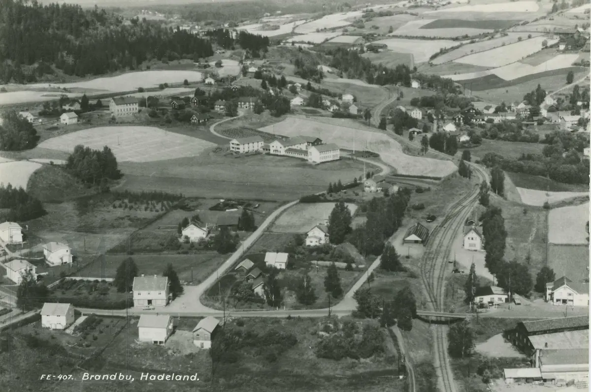 Brandbu sentrum vest. Bak fra venstre: Vesttoppland folkehøyskole, Skogskolen og Augedals bro. Foran fra venstre: Bentestuen butikken, Brandbu jernbanestasjon, Frogner butikken