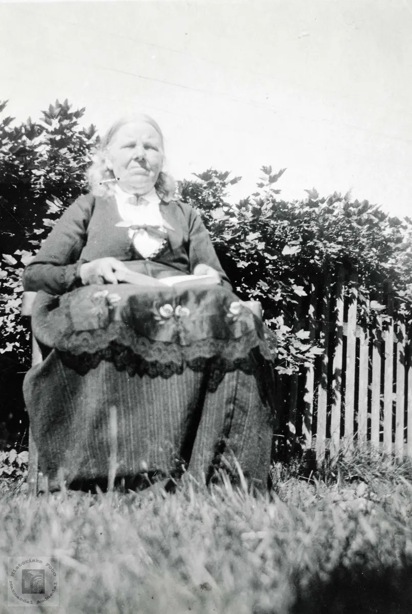 Ingrid Ubostad, f. 1846, har tid til ei lesestund i hagen på Ubostad. Grindheim Audnedal.