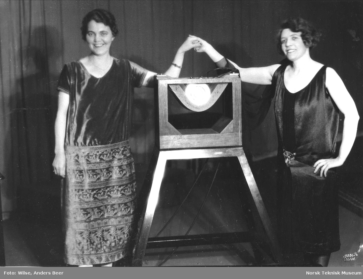 Petra Henriksen og sangerinnen Magda Blanche Mauclaire poserer på hver sin side av den første Marconi-Sykes dyn mikrofonen (museumsnummer 173, defekt, bedre eksemplar gitt NTM) i Studio A, Kringkastingselskapet A/S, Stortingsgaten 26