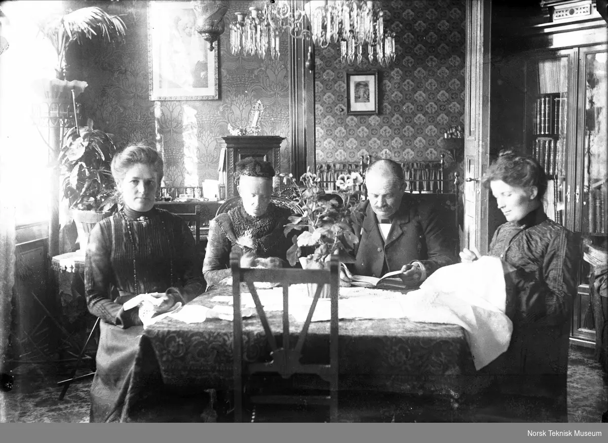 Tre kvinner og en mann i stueinteriør (kanskje Lars Engebretsen som grunnla Kampens mekaniske verksted i 1865)