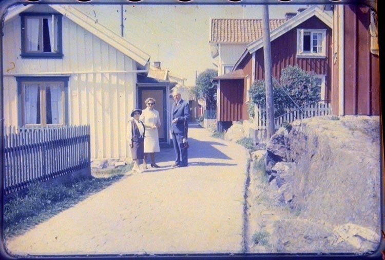 Alfred och Signe Andersson med väninna, på utflykt. Flera bostadshus syns på bilden. Staket syns på sidan av vägen.
Okänt var, troligen Mollösund, Bohuslän.