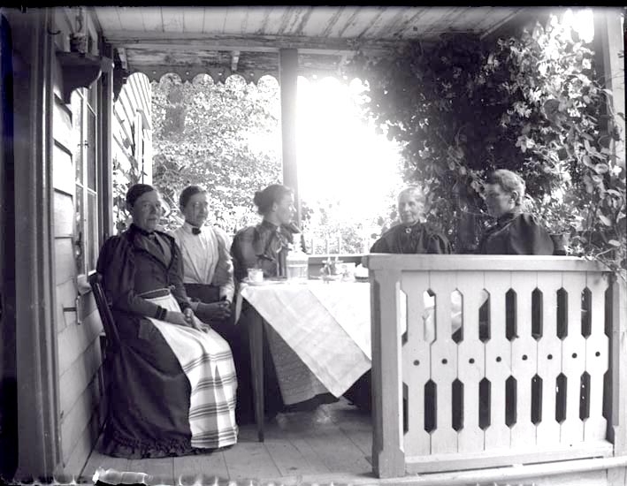 Fem kvinnor sitter på en veranda och dricker kaffe