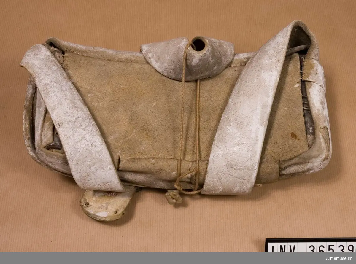 Patronväska av vitt sämskat läder.
Inuti patronväskan finns en bleckplåtsinsats med rum för 12 patroner av ca 18 mm kaliber. Ett par rör saknas och under locket finns en extra ficka.