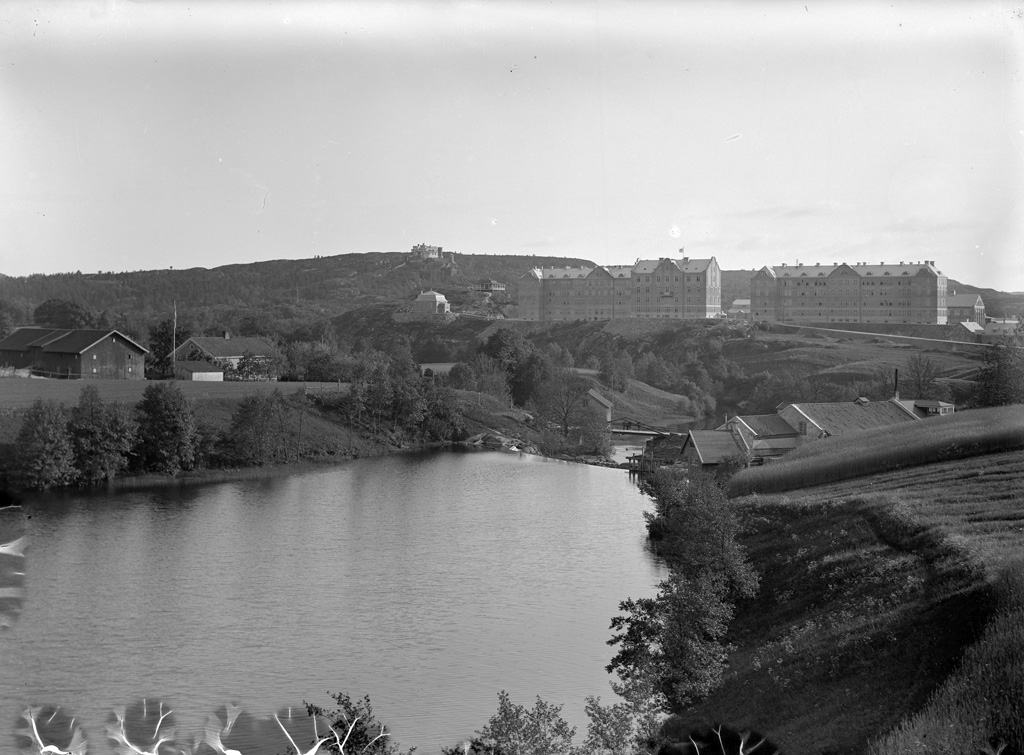 Text till bilden: "U-a Regemente".

I förgrunden utmed Bäveån skymtas till höger Fossumbergs kvarn och till vänster om ån vid bron, Fossums kvarn. Till vänster om kasernerna finns musikberget med det första marketenteriet som användes fram till 1918 och något mer till vänster musikpaviljongen. På höjden i bakgrunden Ture Malmgrens borg som byggdes under åren 1899-1912