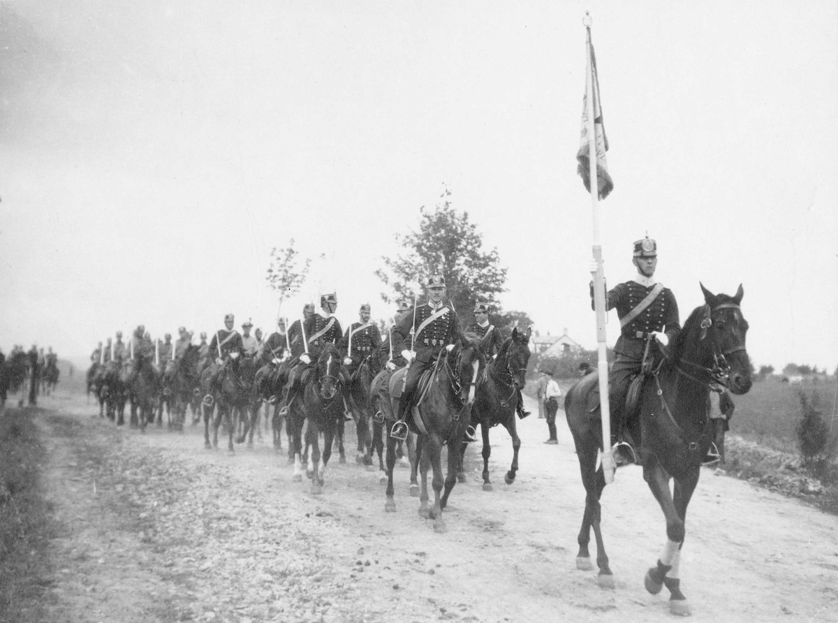 Wendes artilleriregemente A 3 rider på lerig väg vid Näsby Rinkaby, 1924, några åskådare tittar på i bakgrunden. Soldaten längst fram för A 3 standar. Soldaterna bär uniform m/1872 och 1910.