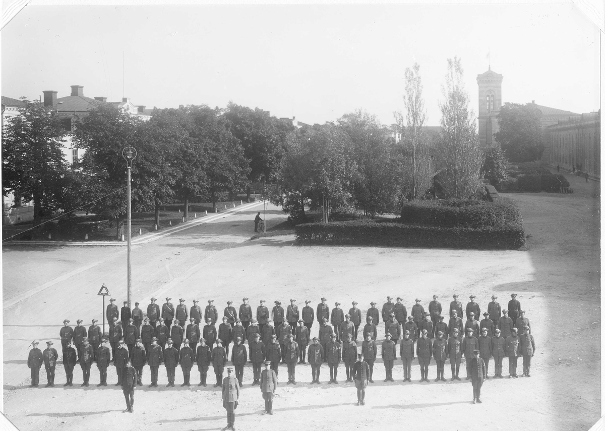 Soldater ur Karlsborgs artillerikår A 10 uppställda på kaserngården 1930. Soldaterna bär uniform m/1886, m/1910 och m/1923. I bakgrunden en man som leder en cykel.
