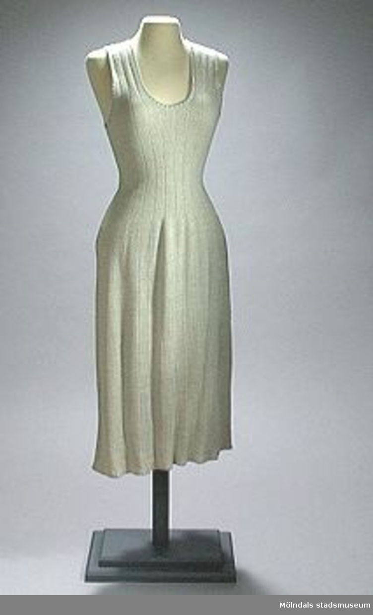 Ärmlös, ljugrå underklänning med axelband. Ingen egentlig urringning. Något utställd kjoldel. Tyget är elastiskt på tvären, eftersom det är resårstickat.Ryggbredd: 300 mm.