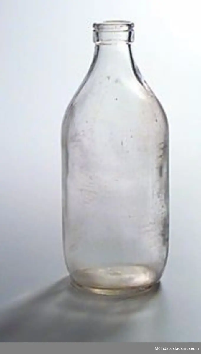 En genomskinlig mjölkflaska i glas. Saknar lock. I botten står inpressat "S" med stjärnor omkring, samt "57" och "1 LIT".