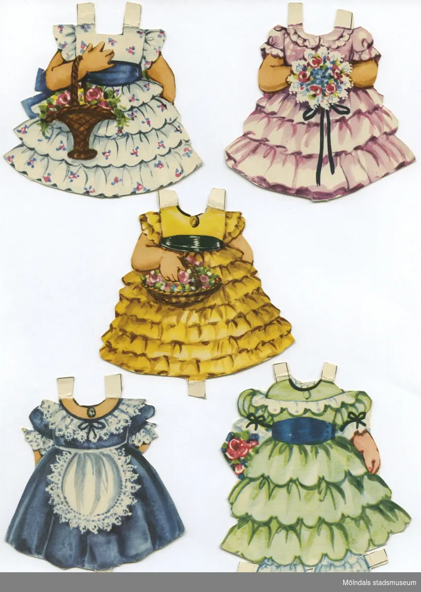 Pappdocka med kläder från 1950-talet. Docka och kläder är märkta "Henriette" på baksidan - dockans namn. Dockan föreställer en liten flicka med blont hår och hårband, iklädd underklänning och mamelucker med volanger, samt skor med vita damasker. Garderoben består av tolv klänningar och en nattsärk i 1800-talsstil. Docka och kläder förvaras ihop med annan docka (MM 04669), i ett brunt kuvert, märkt med blyerts "4 år Annika", men är ursprungligen från "KF Konsum - hushållens förening för lägre levnadskostnader". 