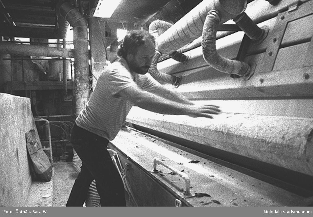 Juris Kuvalds arbetar vid ett  bestrykningsverk för kartongtillverkning i Byggnad 6, 1980-tal. 
Bilden ingår i serie från produktion och interiör på pappersindustrin Papyrus.