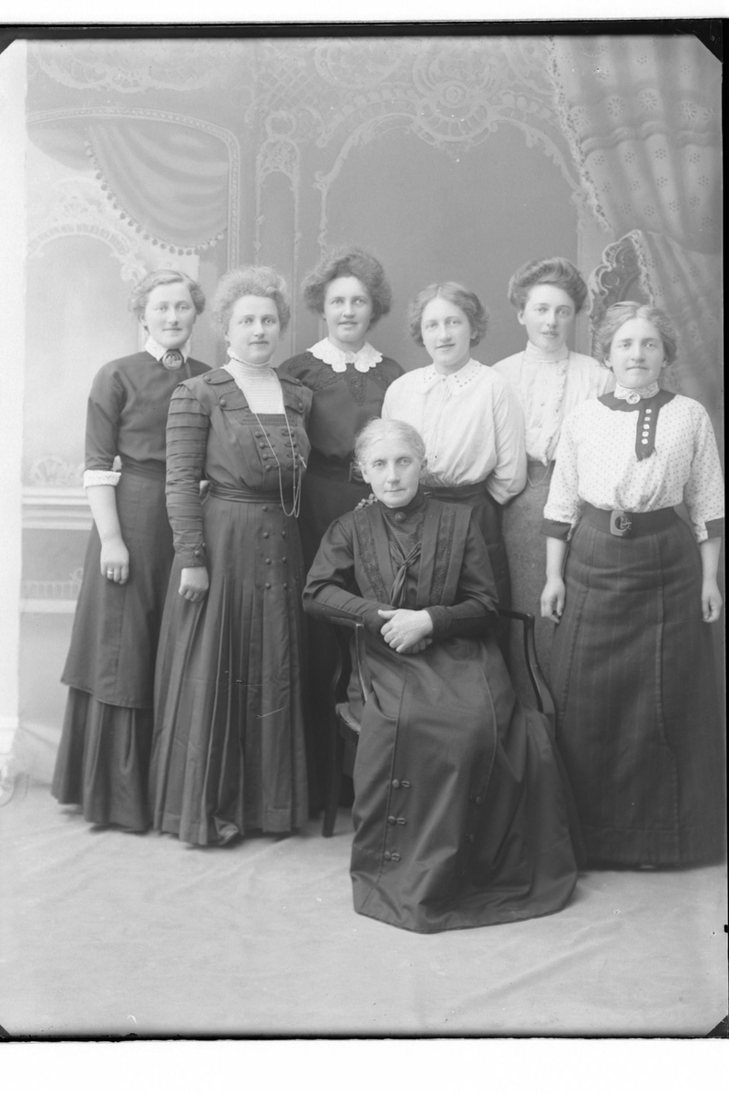 Gruppeportrett av syv kvinner. En eldre kvinne sitter i en stol, mens seks yngre kvinner står bak henne.