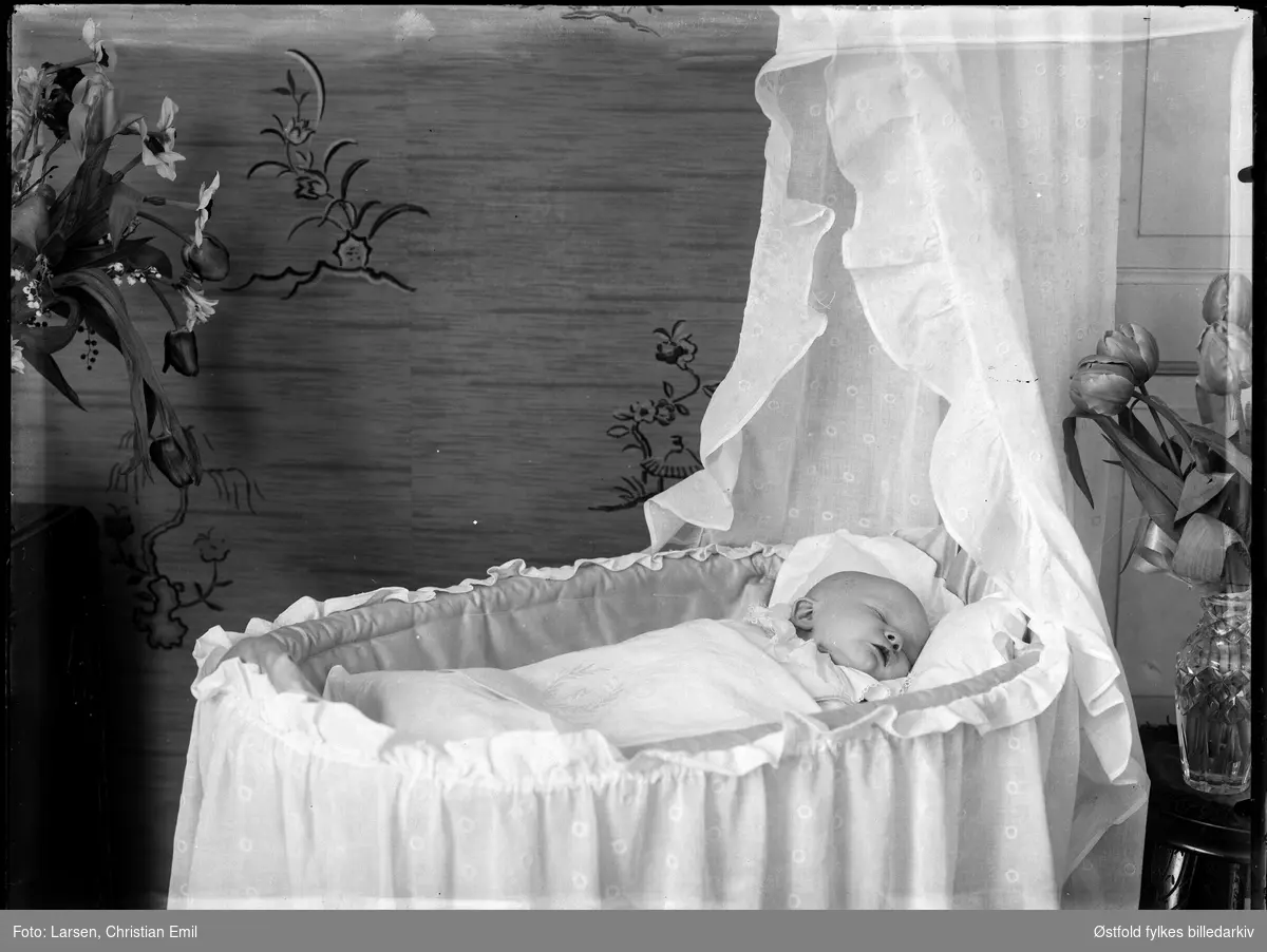 Baby i babykurv med himmel.. Blomsterdekorasjon på tapet, ant.  post mortem-portrett? 1935. Vase med tulipaner på bord. Til venstre bukett med tulipan, lilje og liljekonvall.