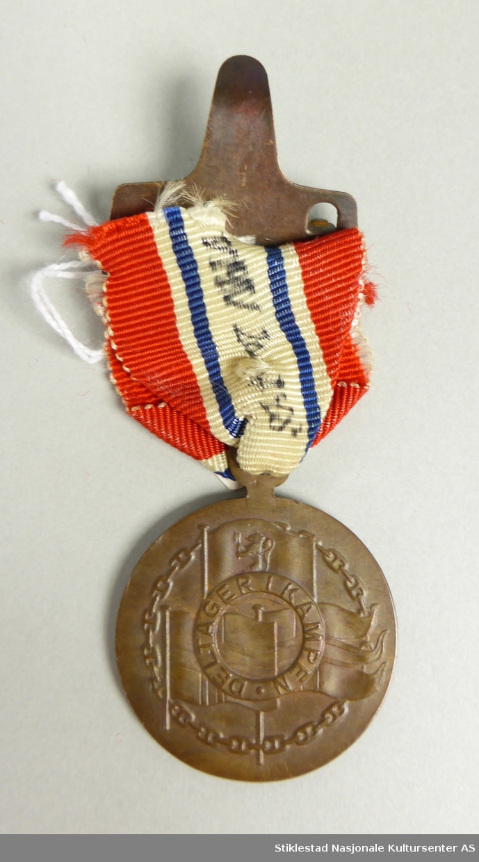 Medalje i bronsje med nasjonalfarget sløyfe/bånd. På forsiden er det et våpenskjold med inskripsjonen 9. april 1940 – 8. mai 1945. 
På baksiden er det kongelige flagg (med riksløve), det norske flagg og nasjonalflagg (splittflagg). Over disse en smal sirkel med innskriften DELTAGER I KAMPEN. Bildet er omgitt av en kjede/kjetting. All dekor er støpt i relieff. Over sløyfe/bånd er det festet en bronsehempe med nål. Bakside stemplet Otto Staup. Sløyfe/bånd er noe defekt (løs fra hempe).