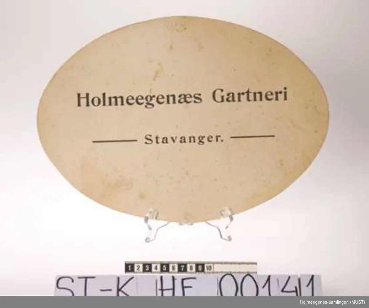 Seks identiske, ovale pappskilt med teksten "Holmeegenæs Gartneri - Stavanger". Antakelig brukt ved butikk- og/eller torgsalg av varer fra gartneriet.