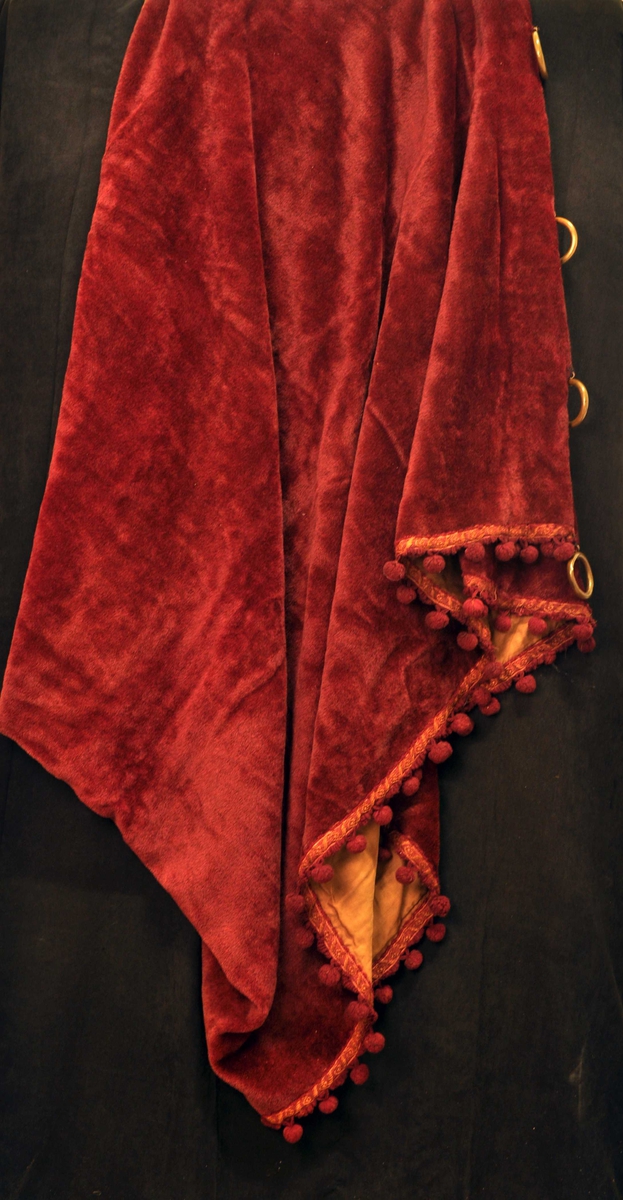 Tykk, mørkerød gardin med gylte opphengsringer, bånd langs kant med mørkerød og gulbrun tråd.