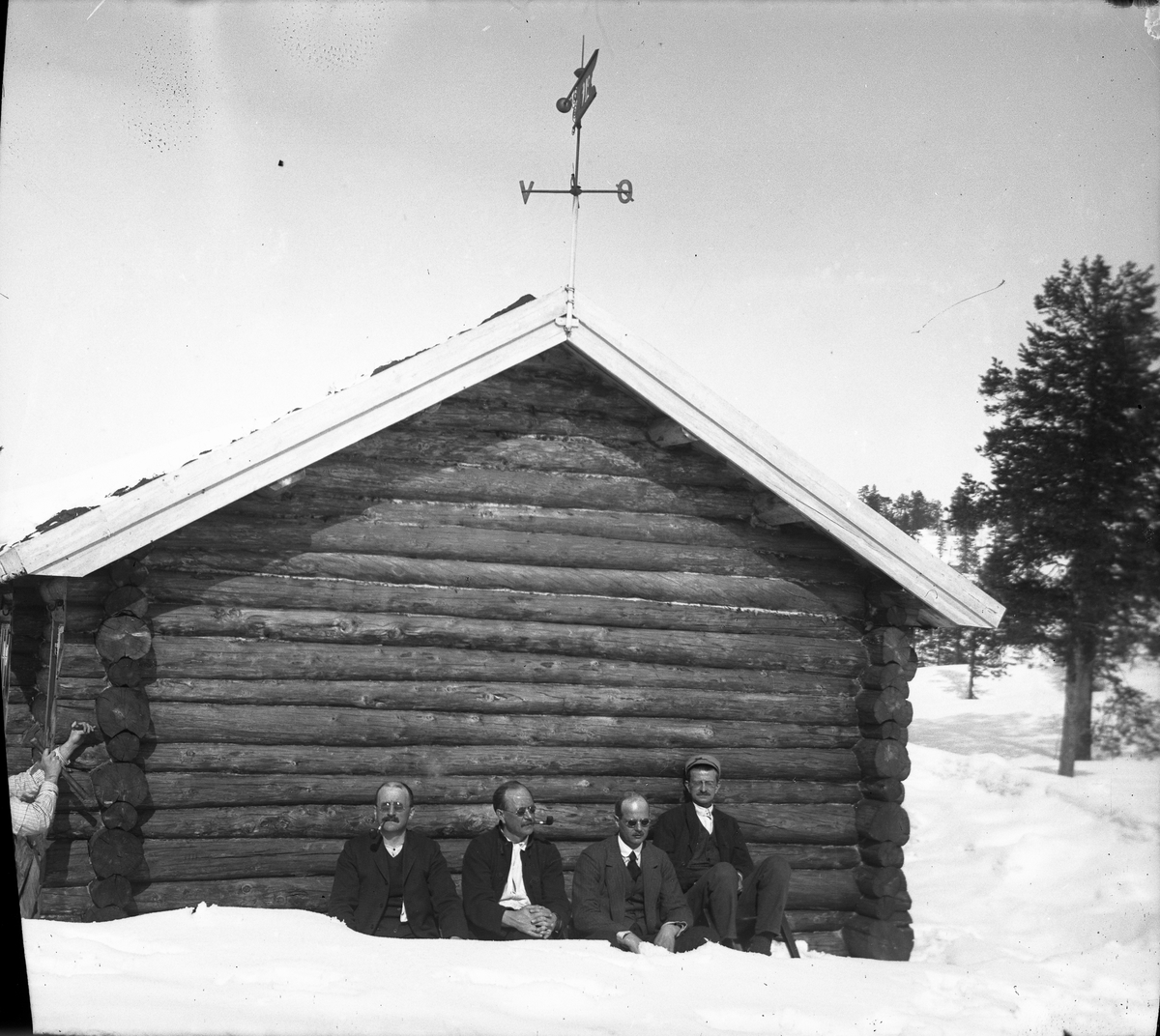 Fire menn ved kortveggen på tømmerhytte ved Måvann, Tørdal