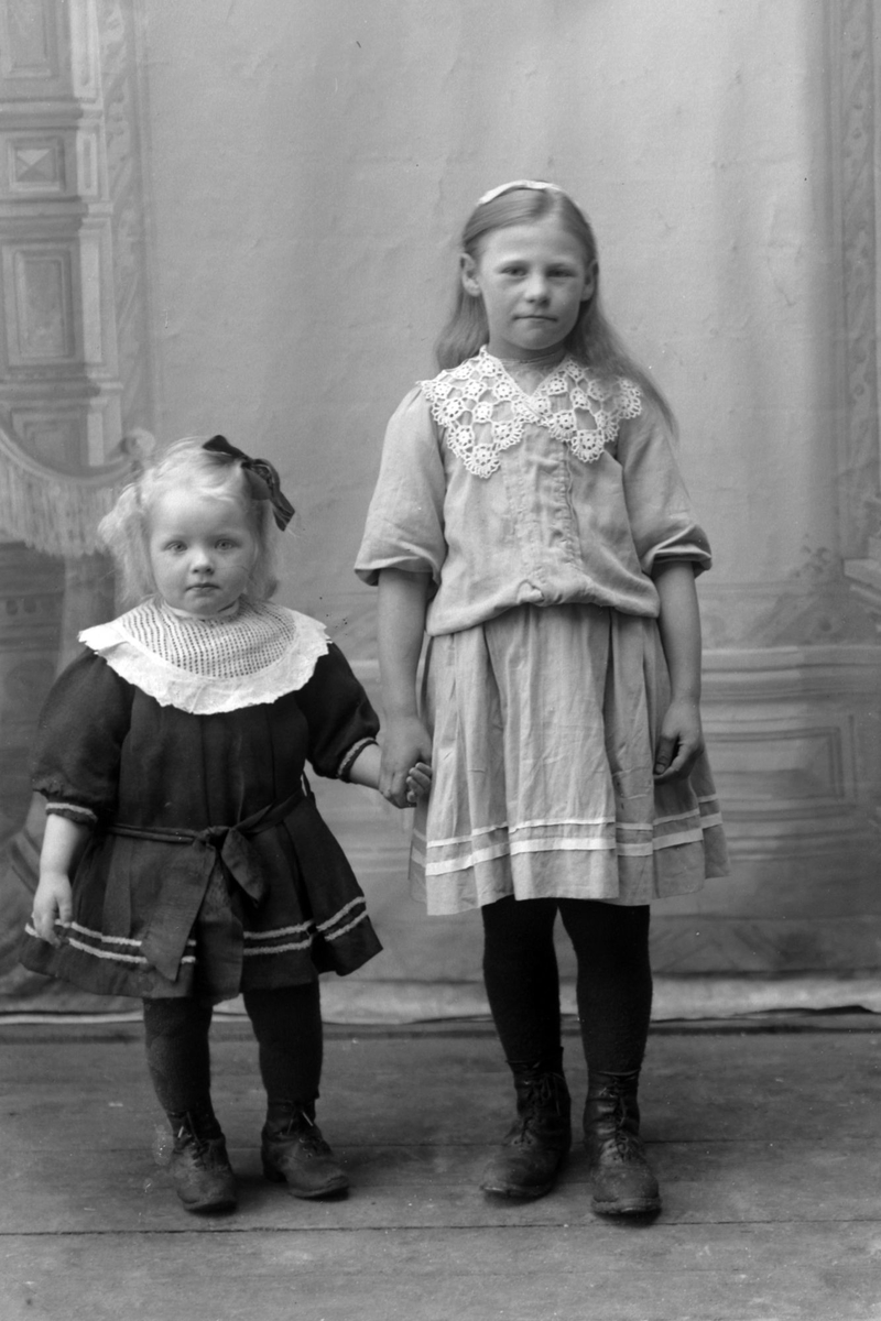 Studioportrett av to unge jenter som holder hender, trolig søstre.