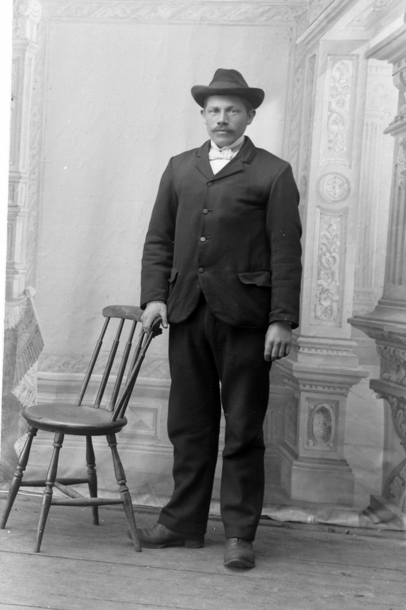 Studioportrett av en mann som står ved siden av en stol.