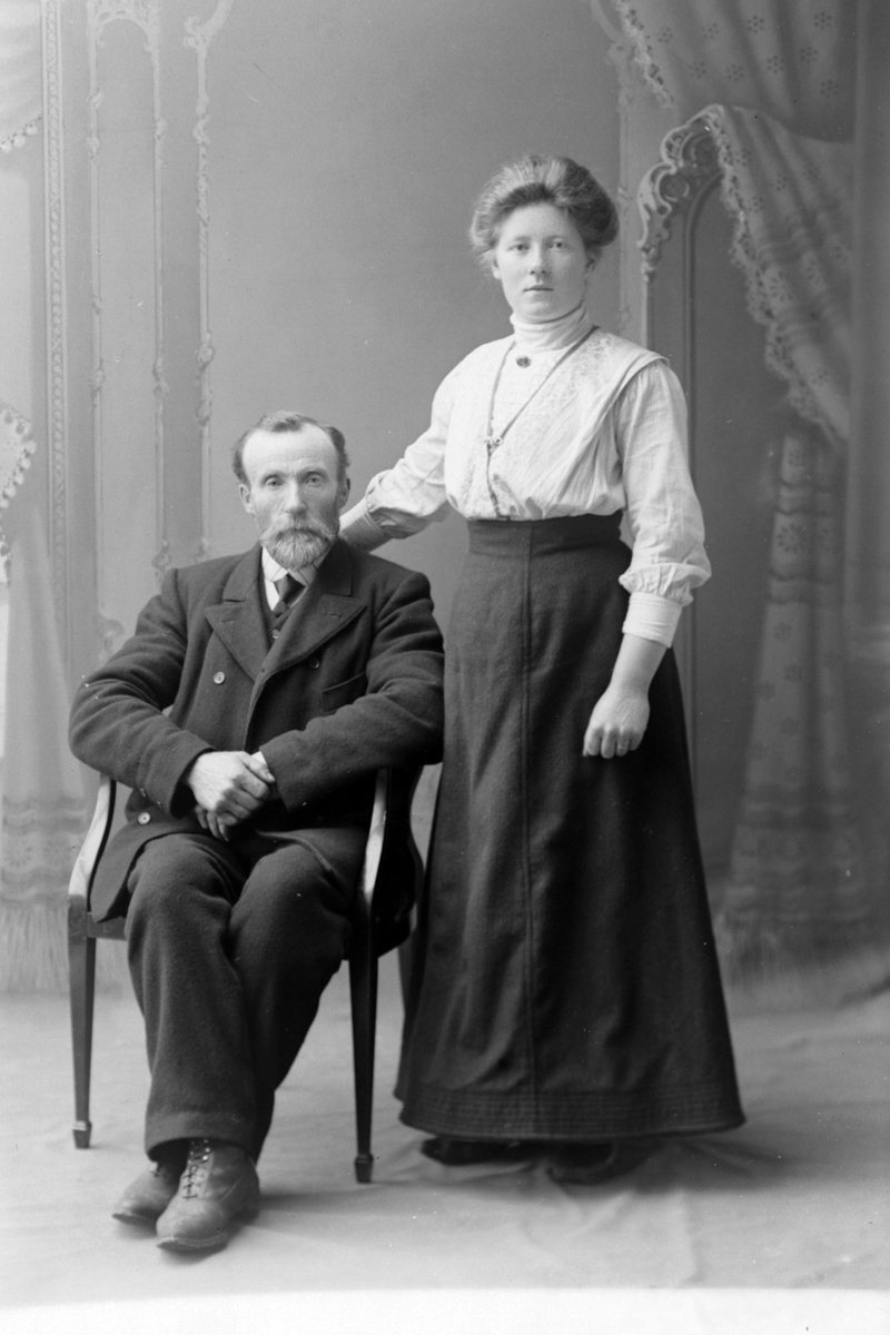 Studioportrett av en sittende mann ved siden av en stående kvinne.