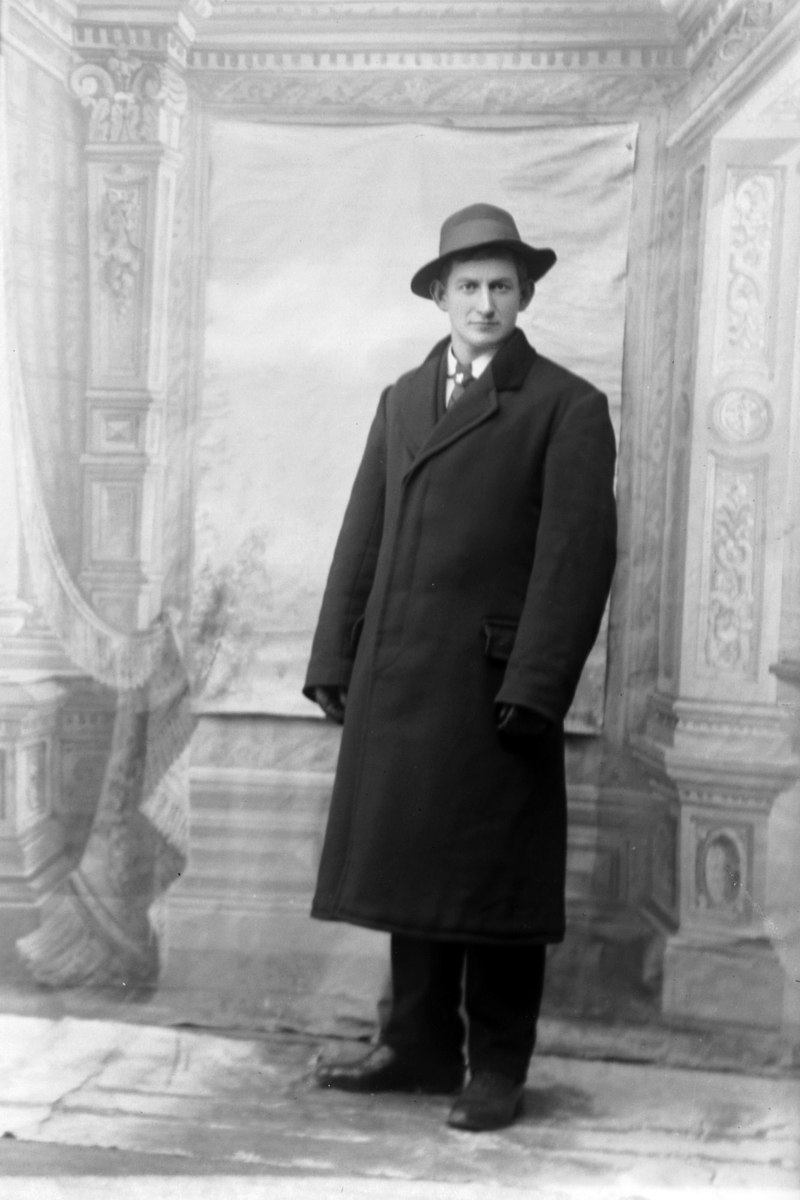 Studioportrett av en mann med frakk og hatt.