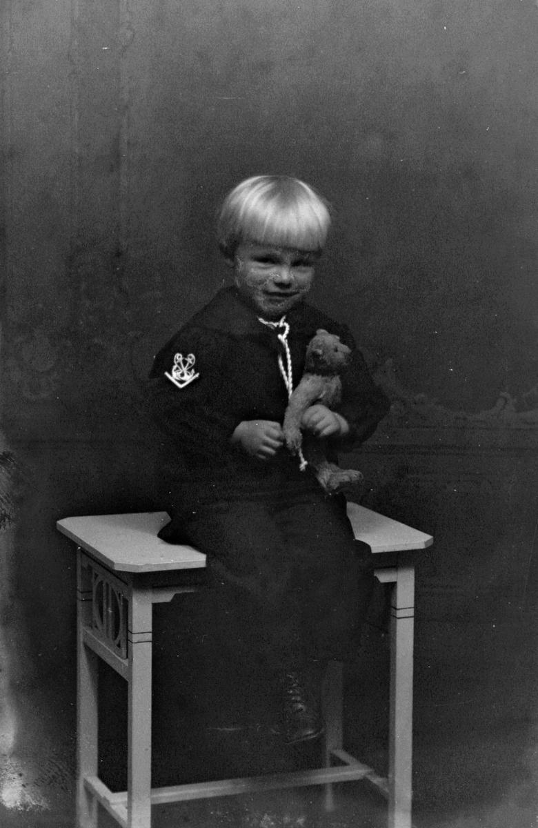 Studioportrett av en gutt i matrosdress med en bamse.