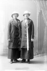 Studioportrett av to kvinner med lange sløyfer på brystet.