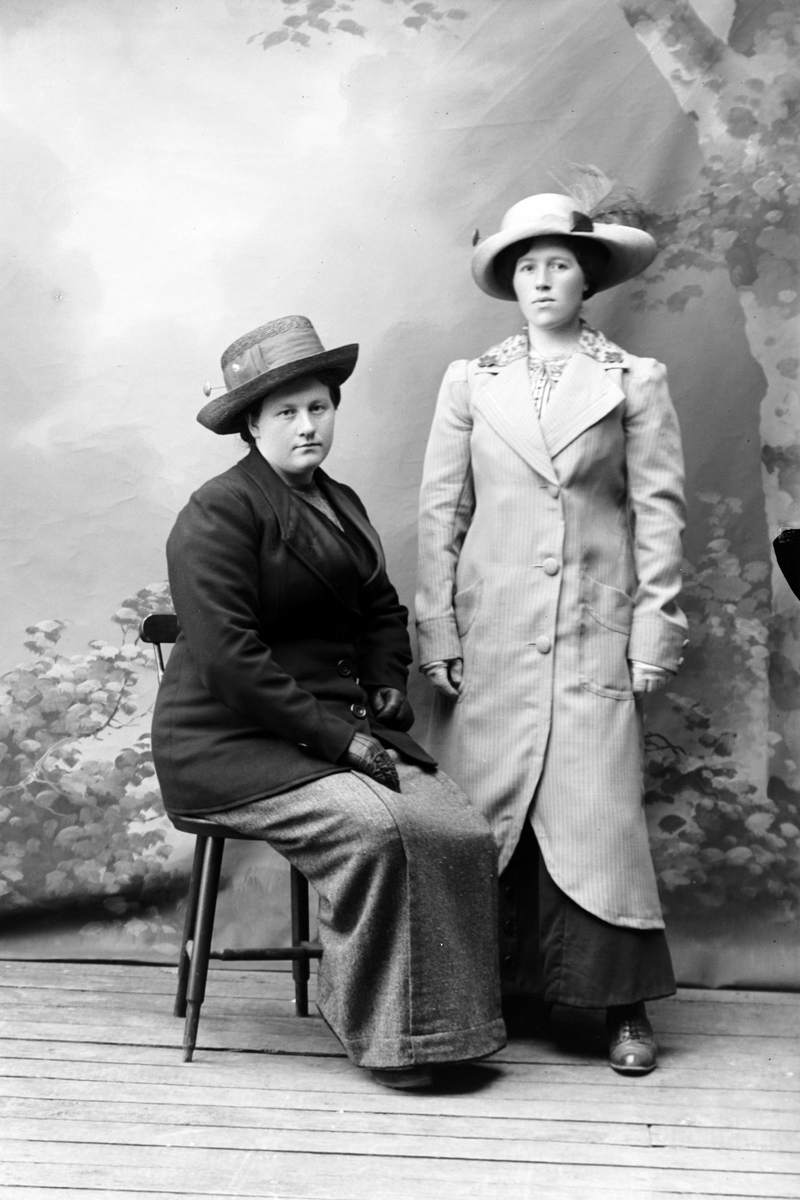 Studioportrett av to kvinner med frakk og hatt.