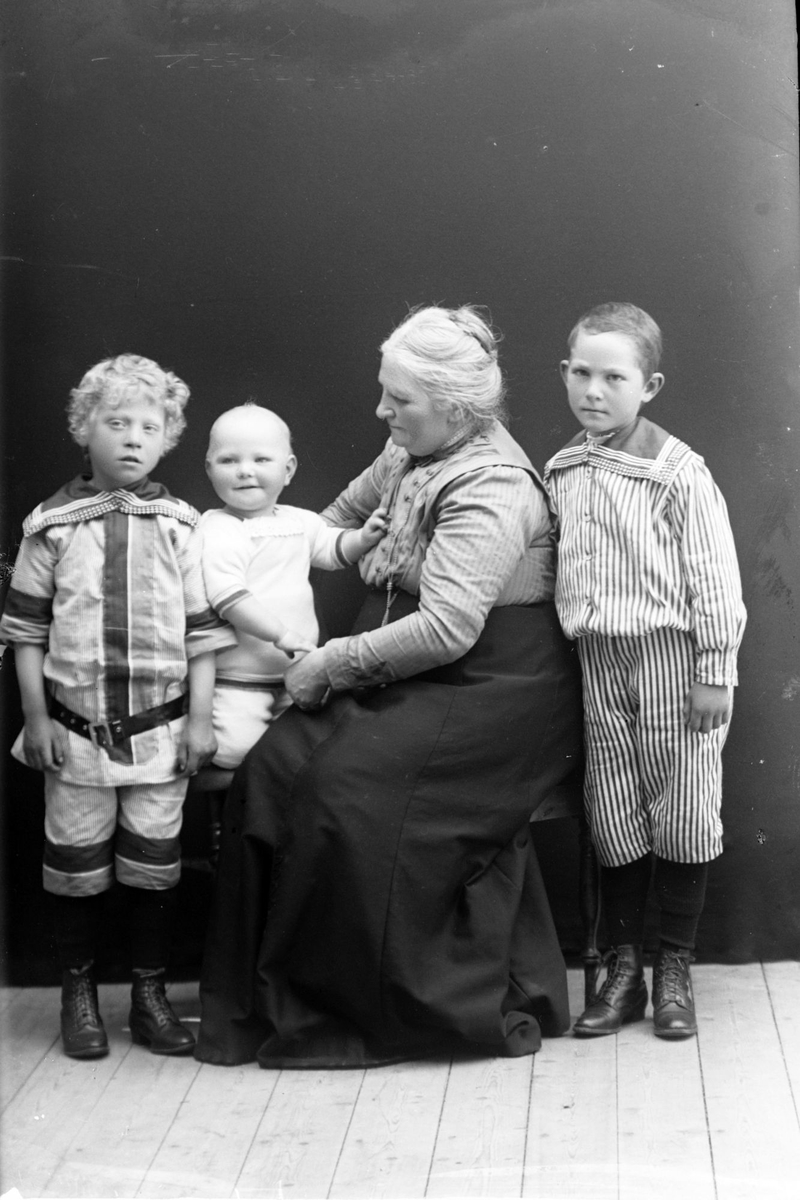 Studioportrett av en eldre kvinne og tre barn i helfigur.