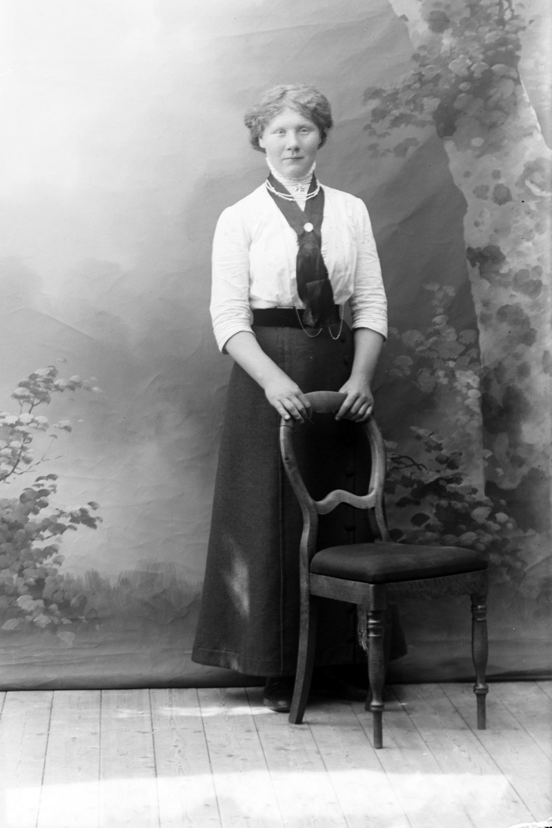 Studioportrett av en kvinne med begge henderne på en stolrygg.