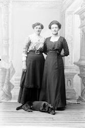 Studioportrett av to kvinner med en hund foran seg.