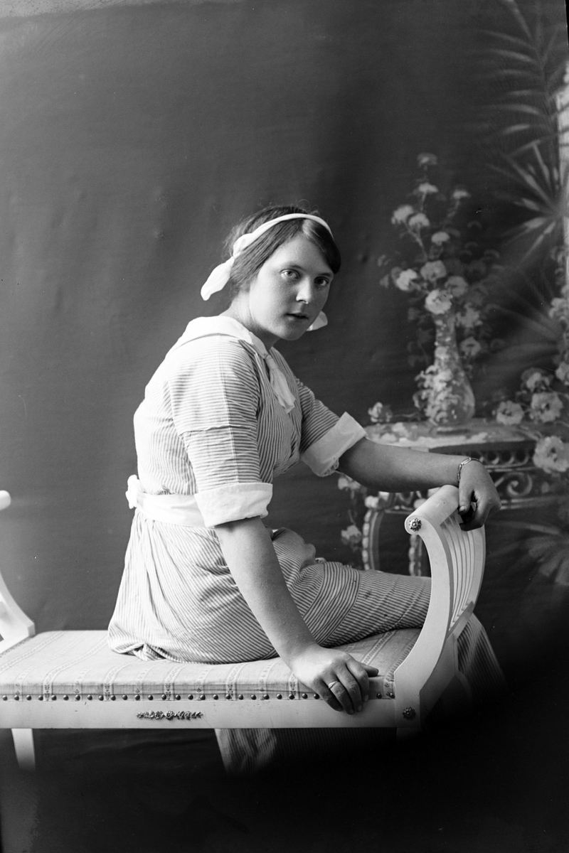 Studioportrett av en ung kvinne sittende på en benk.
