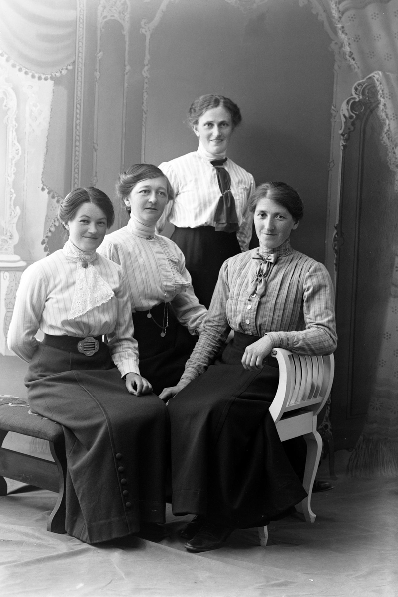 Studioportrett av tre kvinner sittende foran én som står.