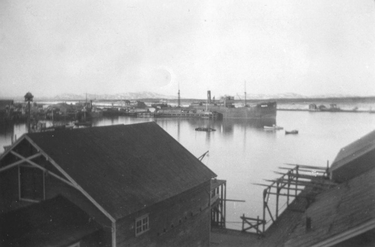 Utsikt over havna i Vadsø. I forgrunnen ses havnebygninger. 'Akka' et skip i tysk fart ligger til kai. Bildet er tatt fra 2.etasje i Evangergården i Havnegaten