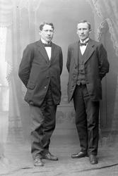 Studioportrett av to menn i helfigur.