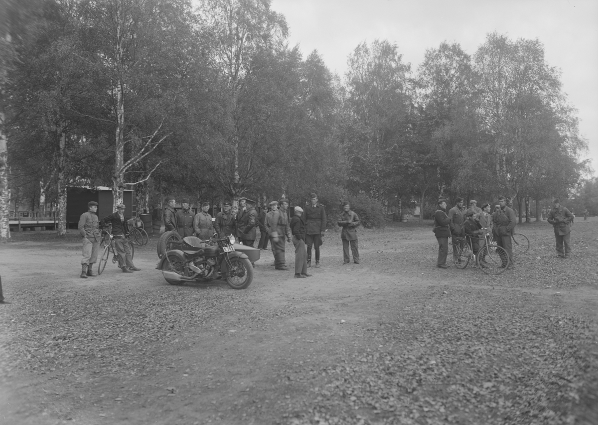 Personal ur andra spaningsdivisionen samlade utomhus vid övning i Rommehed, 1936. Män och pojkar i samtal vid cyklar och militär motorcykel.