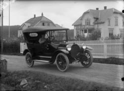 Bil og sjåfør, bolighus i bakgrunnen. Tatt i hesselbergs gat